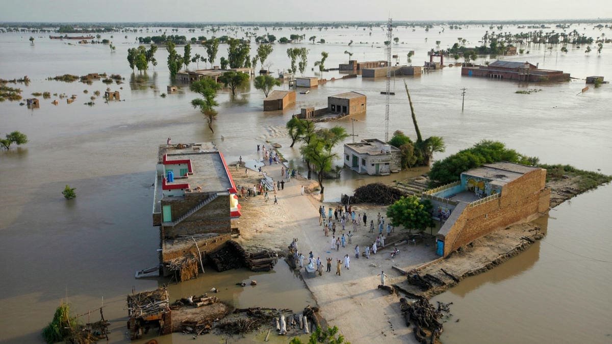 Plan d'ensemble depuis un hélicoptère d'un village inondé au Pakistan.  Des personnes bloquées demandent de l'aide depuis une zone sèche.