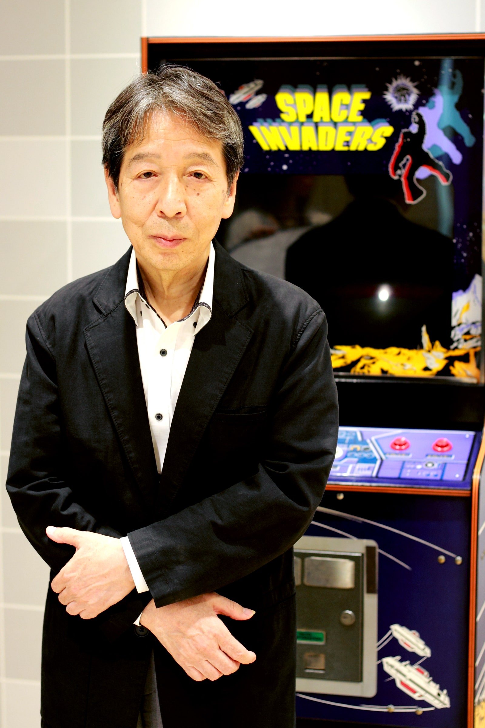 Tomohiro Nishikado posant à côté d'une borne d'arcade Space Invaders