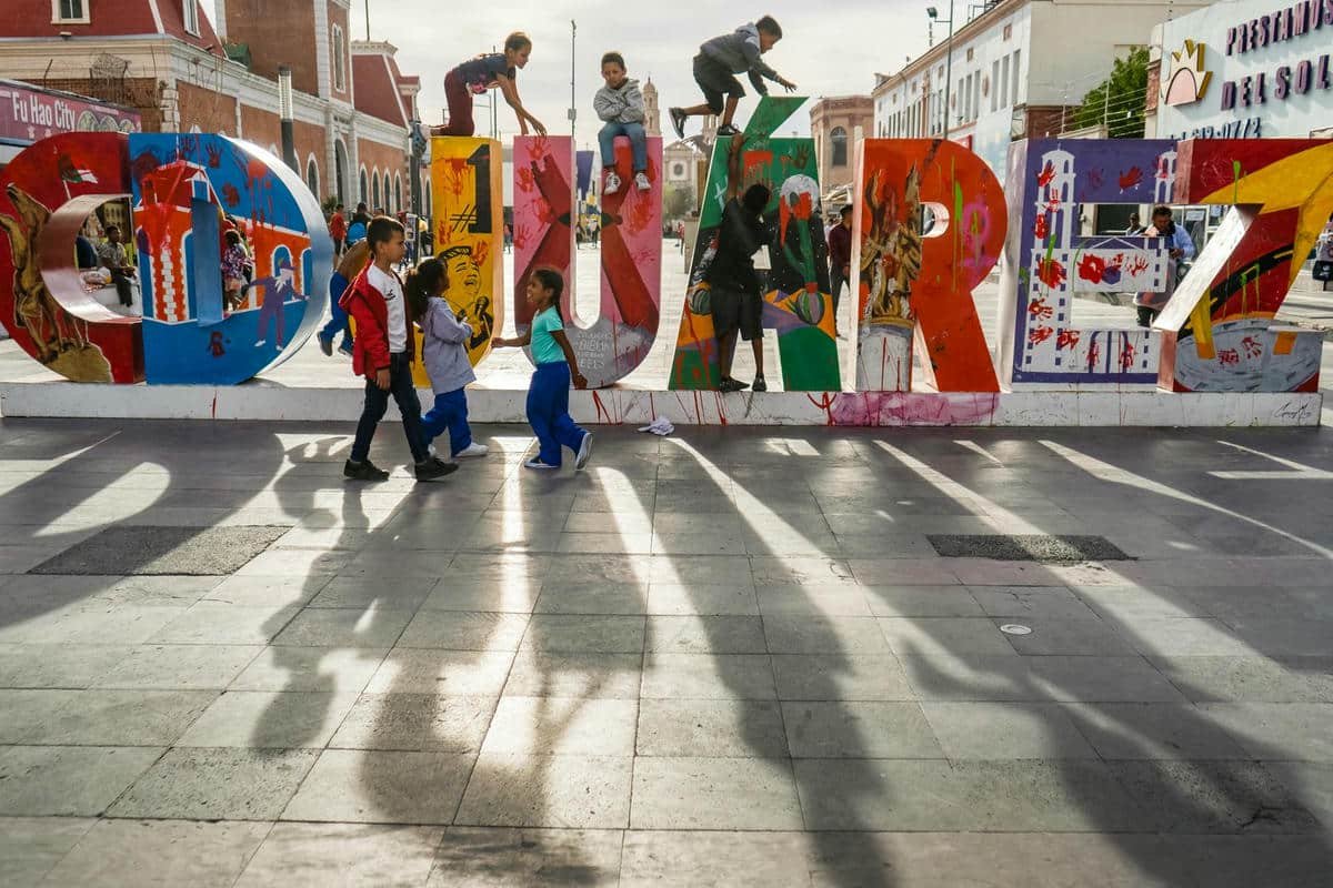 les enfants grimpent sur une sculpture en 3 dimensions de l'oeuvre Juarez.  Le soleil fait de longues ombres au premier plan.