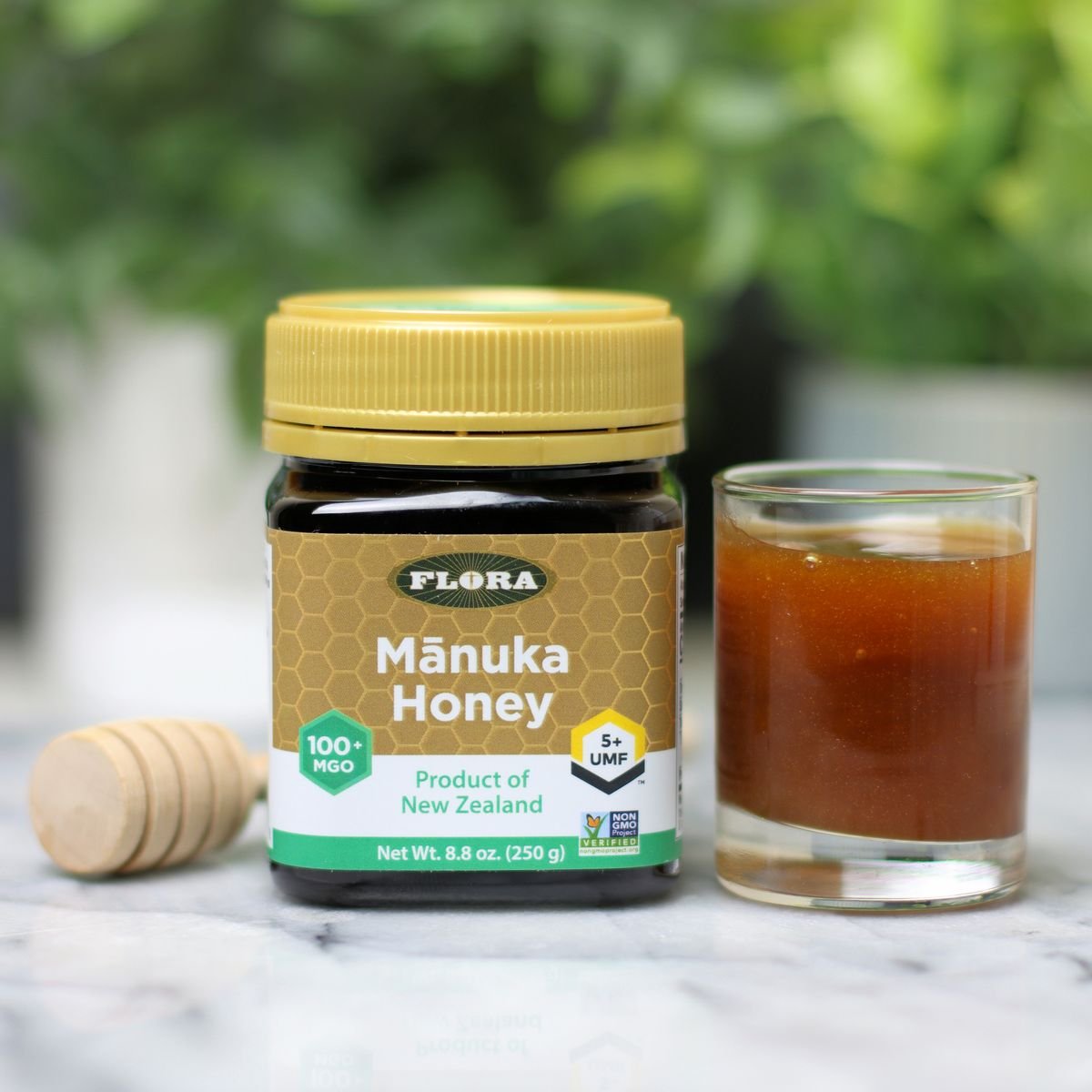 Un pot de miel de Flora Manuka à côté d'une portion dans un bocal en verre