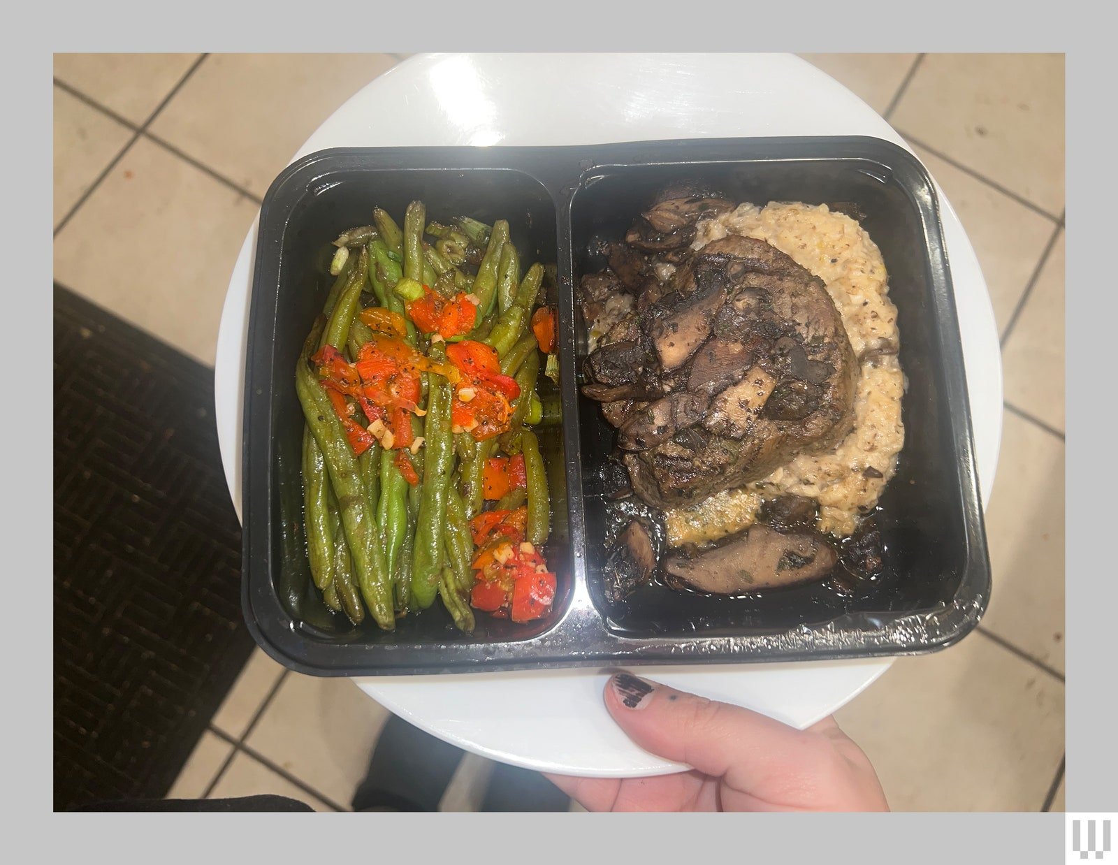 Repas précuit dans un plateau noir segmenté tenu sur une assiette blanche par quelqu'un